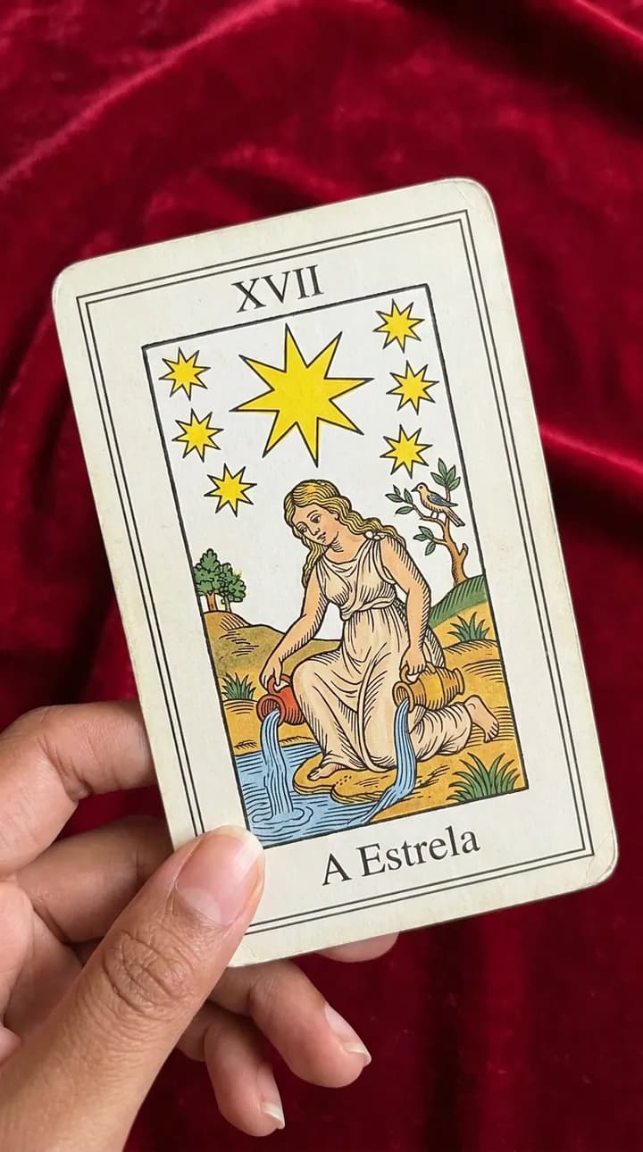 Hand holding The Star card, from the Marseille deck, over the red velvet