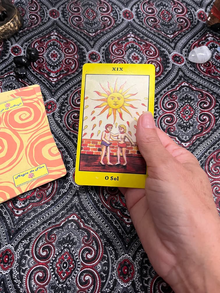 Mão segurando a carta O Sol sobre a toalha da mesa